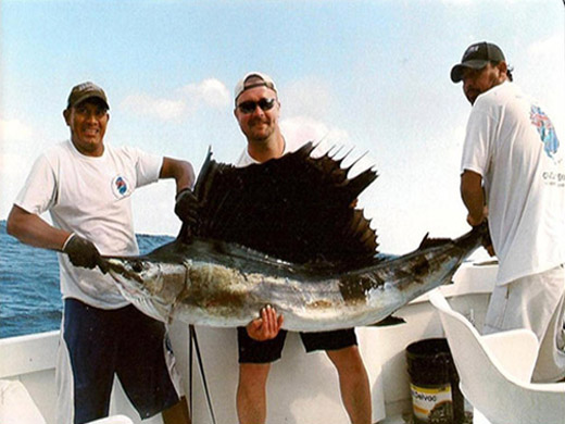 Charter boat passengers smiling while holding a large Atlantic Sailfish before release on the deck of a private yacht