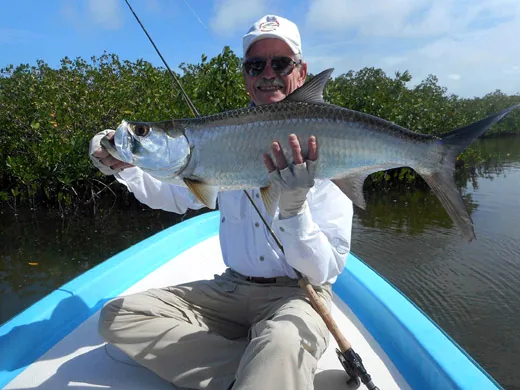 An angler holding a silver baby Tarpon caught on a fly rod in the shallow saltwater flats of Isla Blanca