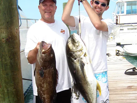 A deckhand displaying a large Black Grouper caught while bottom fishing over deep continental shelf structures in Cancun